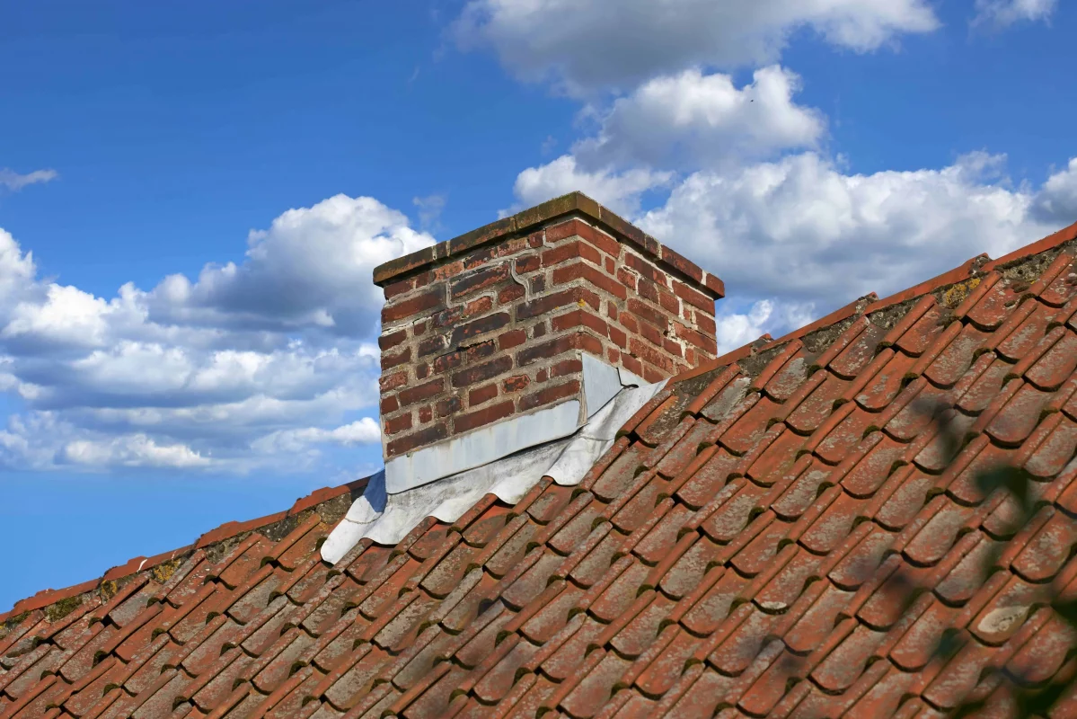 A brick chimney stack with lead flashing on a tiled roof
